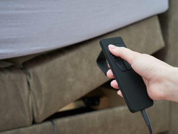 Female hand and remote control to adjust the tilt of the bed mattress, close-up